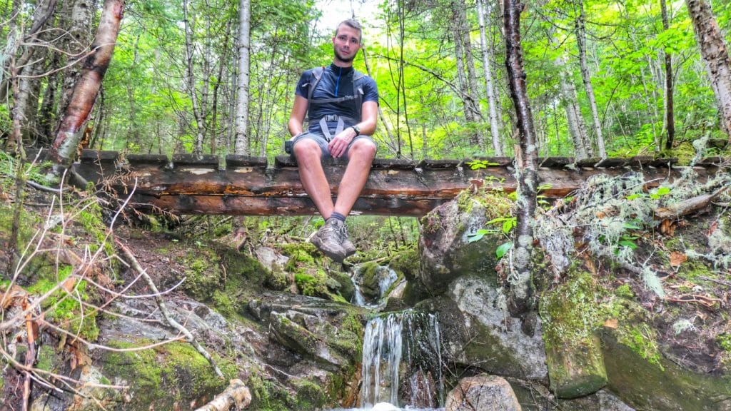 Anthony de Partir Loin assied sur un petit pont au dessus d'un petite chute d'eau dans la forêt des Morios